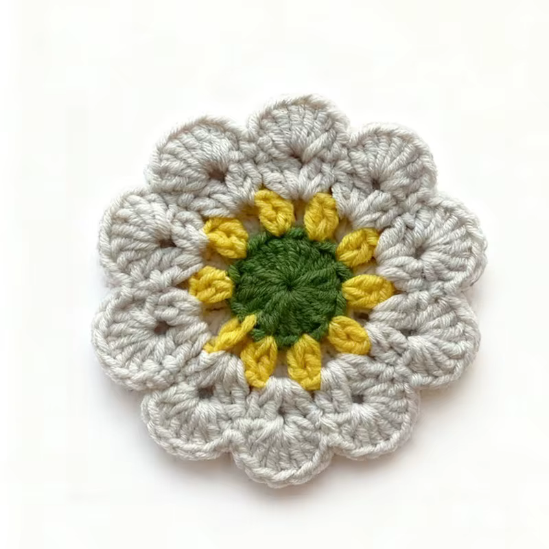 Warm golden crochet flower coaster with olive-green and dusty-rose center details on a white background